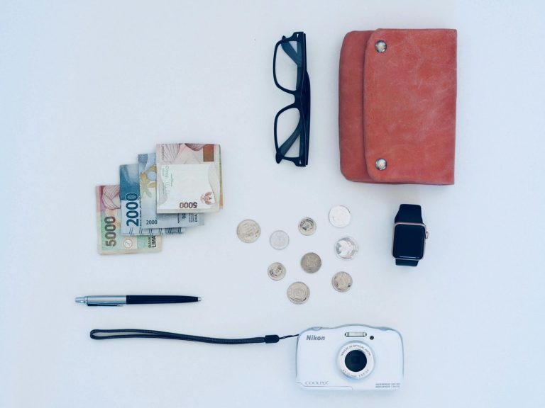 Flat lay of everyday items including currency, coins, wallet, and gadgets, all on a white background.