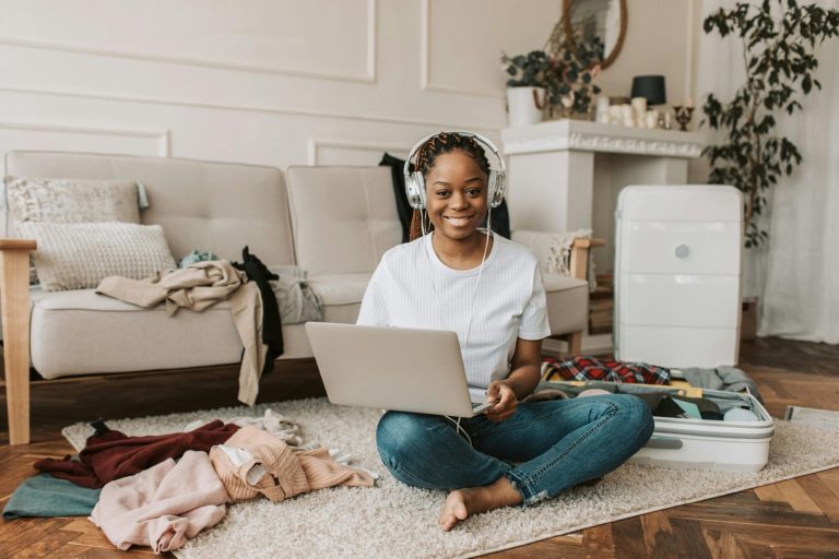 Smiling young woman packing suitcase and using laptop in a cozy living room.